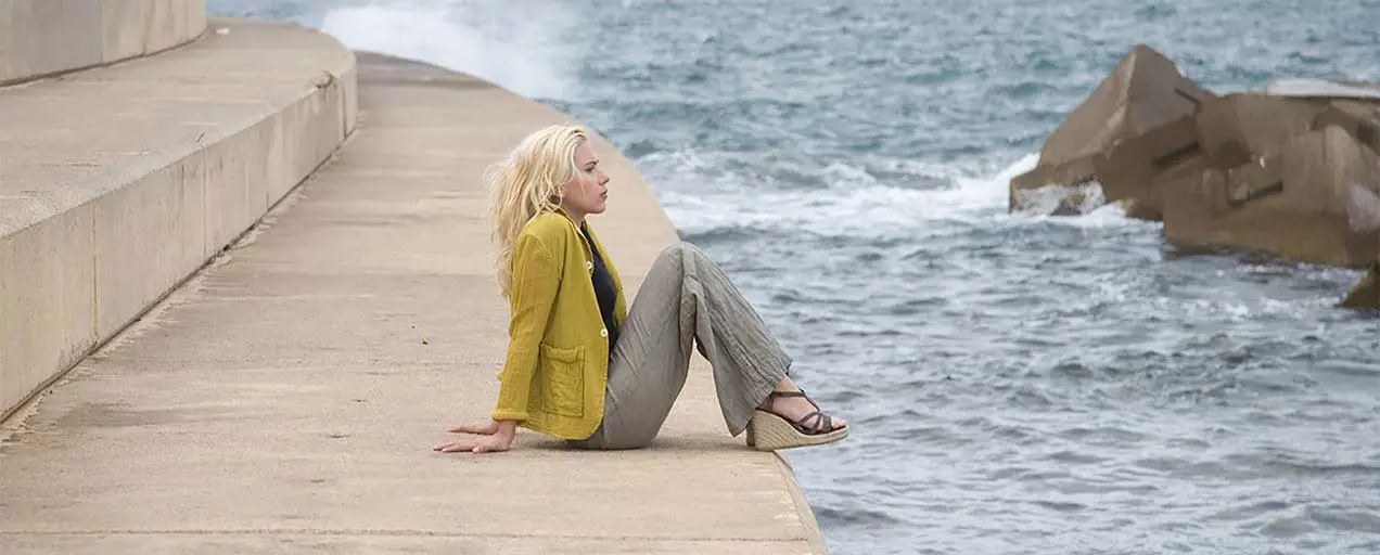 Woman sits by ocean, contemplating.